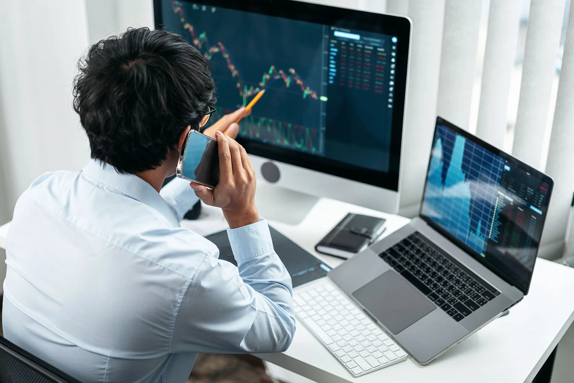 Business professional on the phone analyzing stock trading charts across multiple computer monitors while working at a desk.