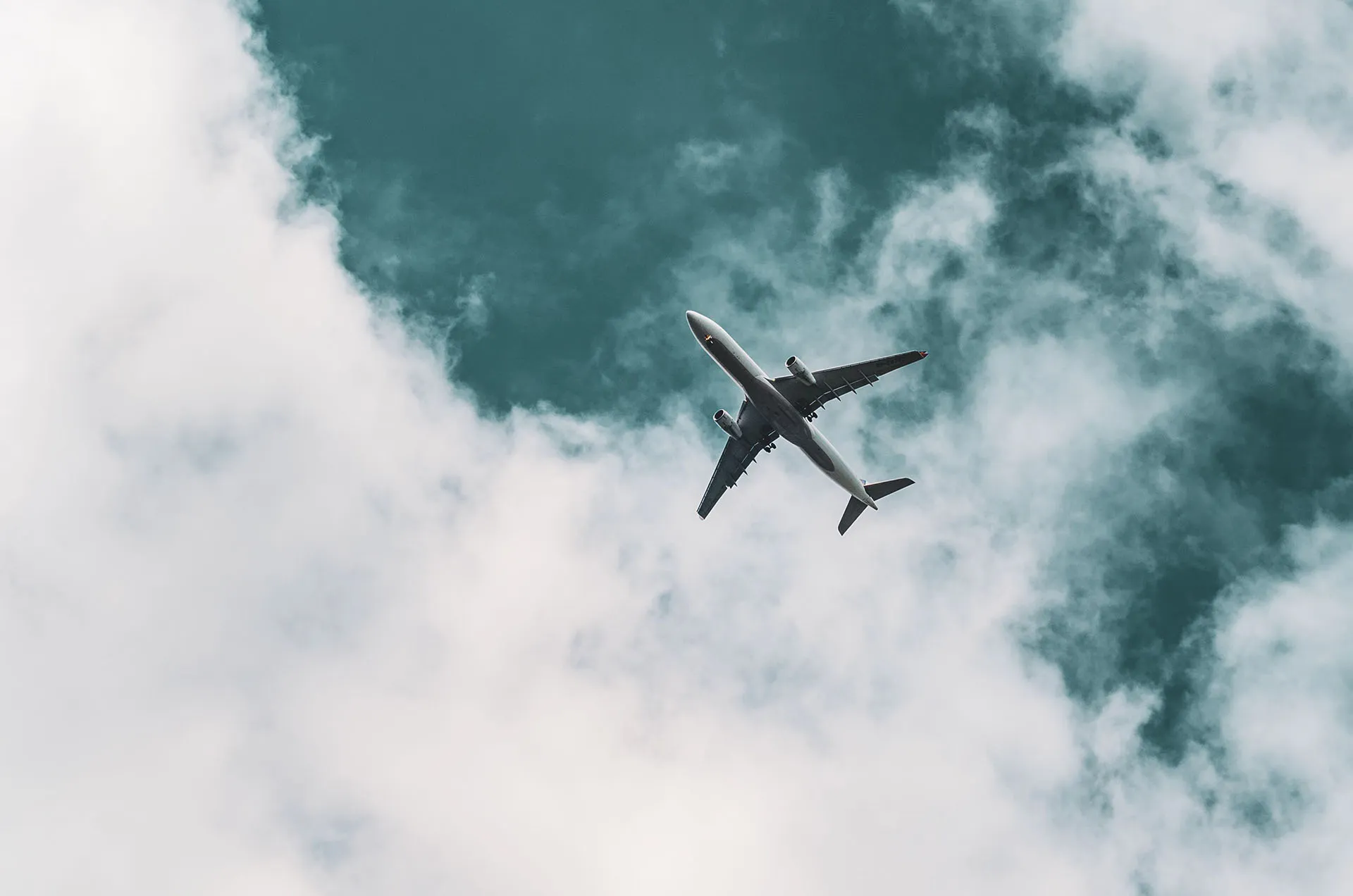Low angle view of an airplane flying through a dark teal sky with wispy clouds
