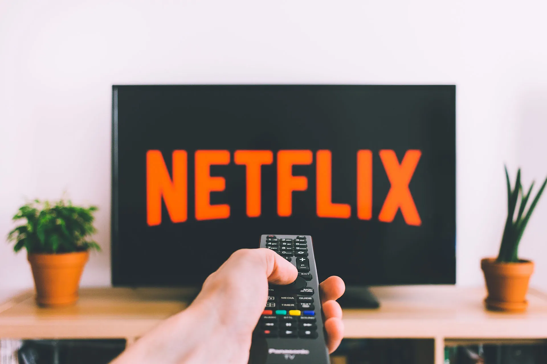 A hand pointing a tv remote towards a tv displaying the Netflix opening screen