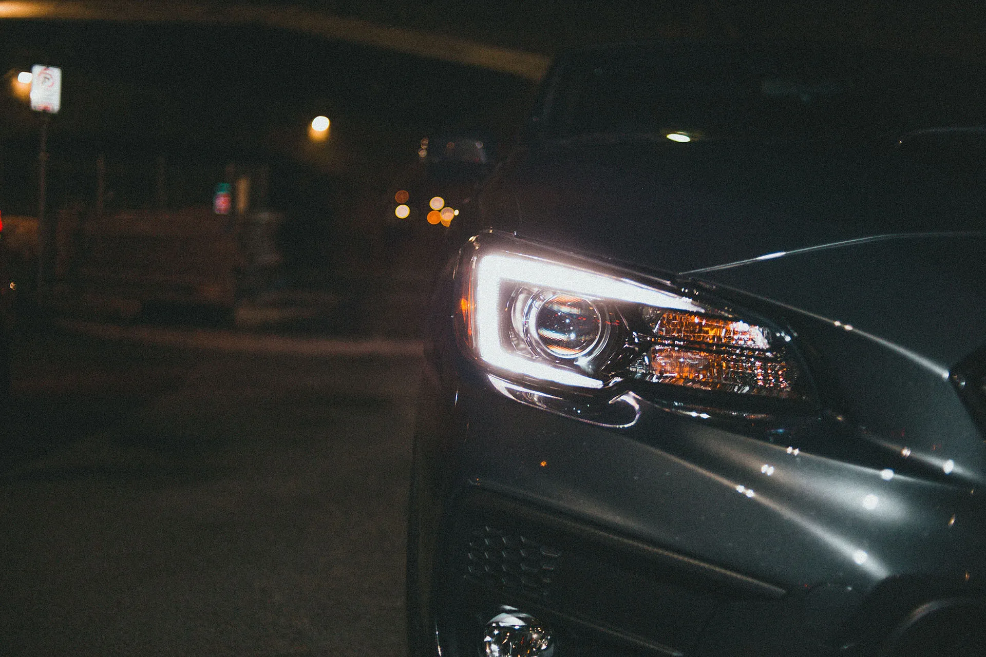  Close up of a headlight and side mirror of a silver car in a dark garage