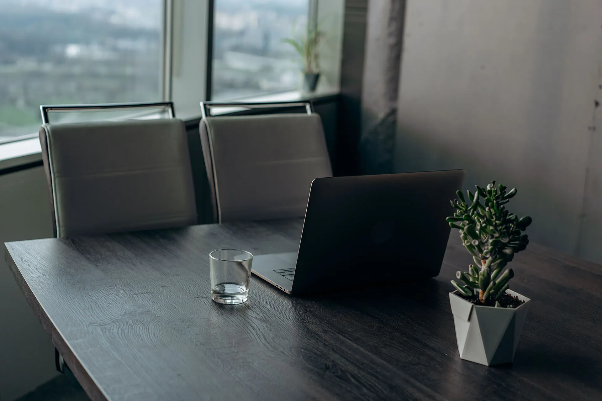 Two office chairs sitting in front of a dark grey wooden table with a laptop and a glass of water in a modern office