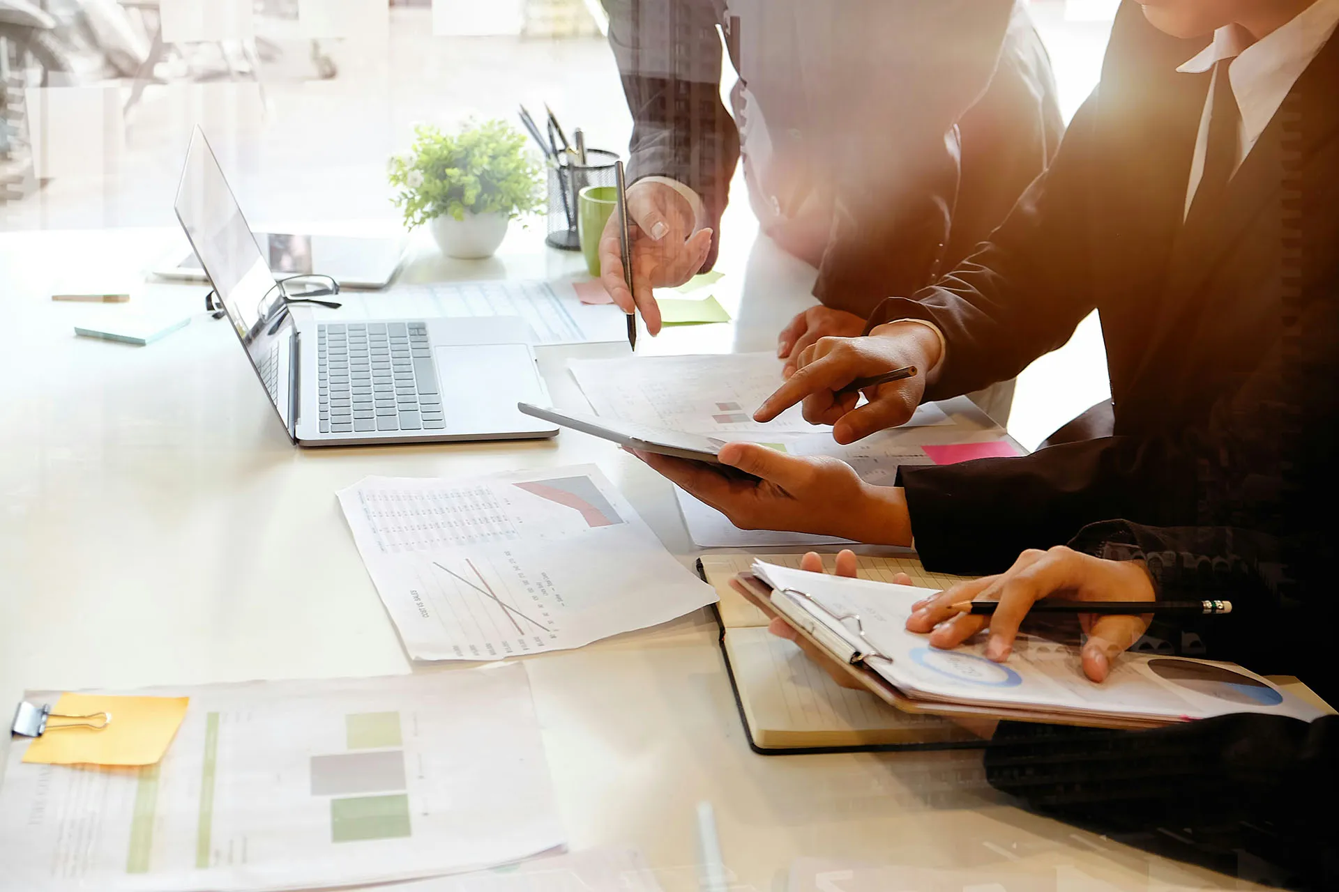  A close-up shot of financial advisors reviewing market trends and data on a tablet and printed reports during a collaborative portfolio review session.