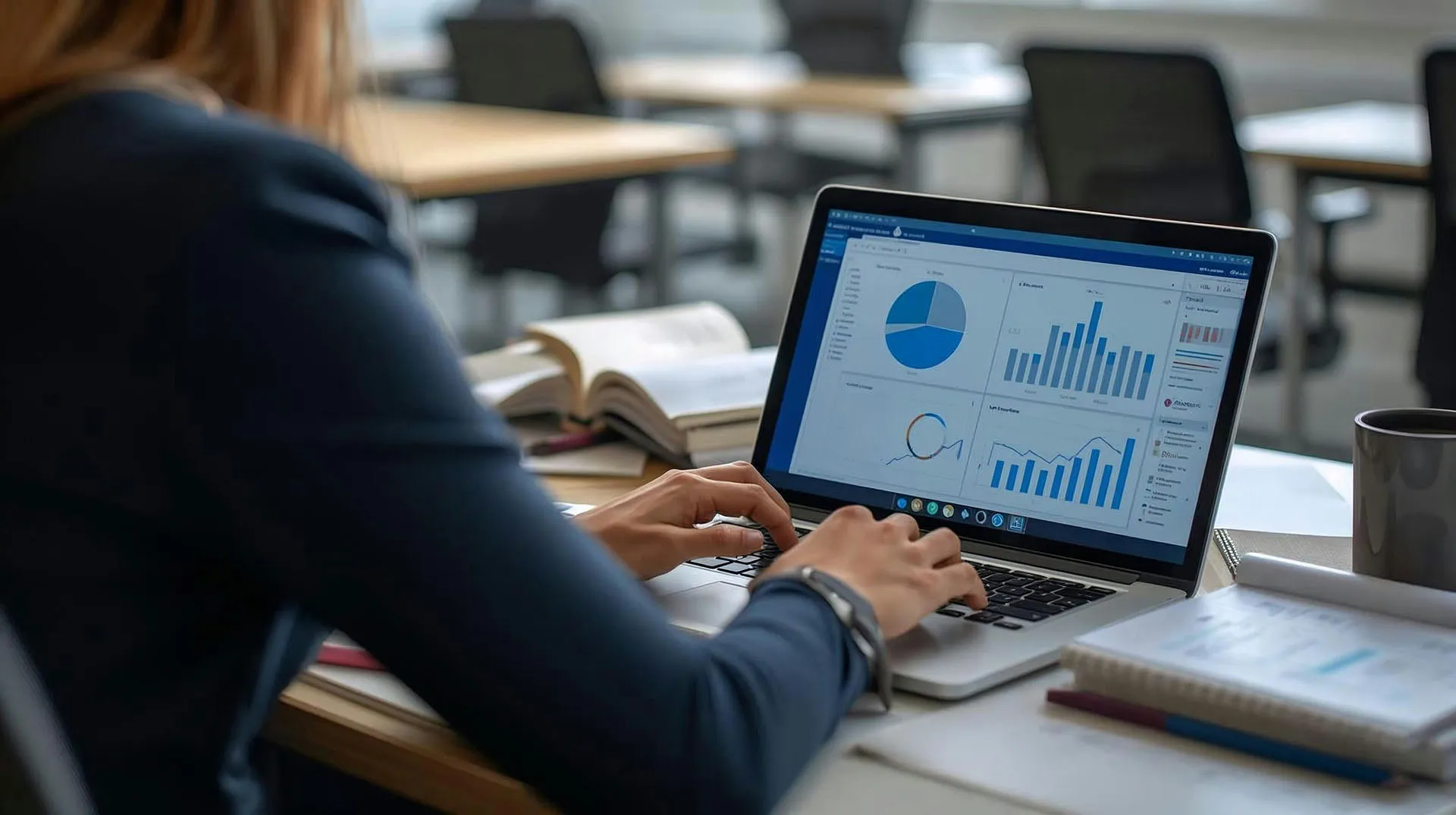  An over-the-shoulder view of a financial professional typing on a laptop that displays a dashboard filled with financial analytics, data charts, and a pie graph.