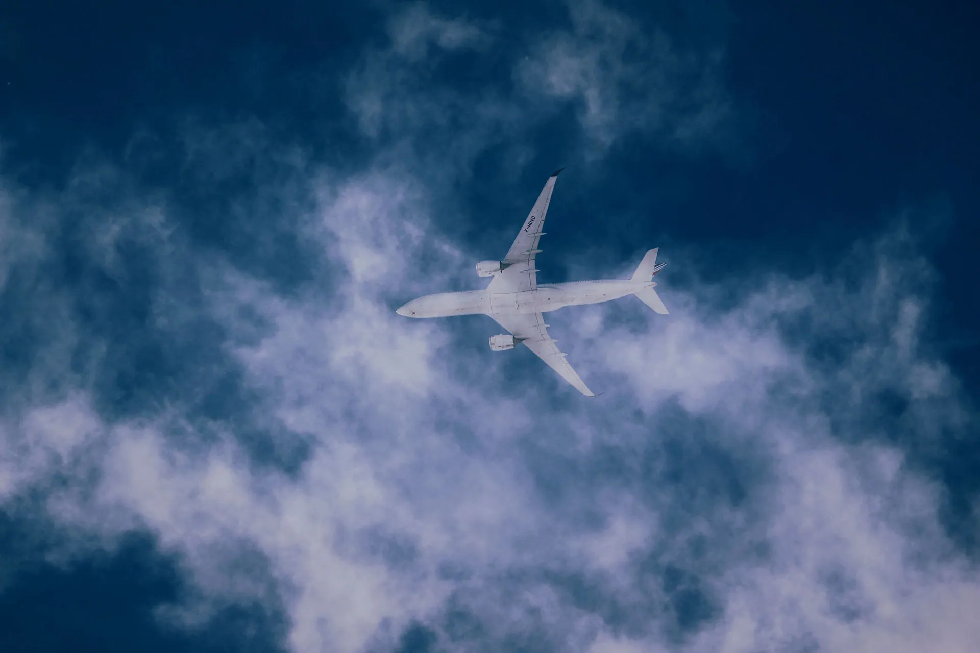  Airplane flying high in a dark blue sky with soft clouds below.