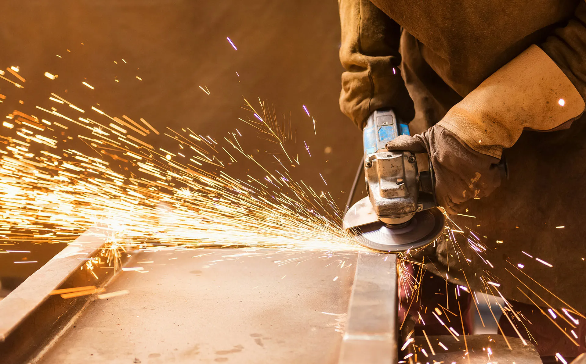  Worker using an angle grinder on metal, sending bright sparks across an industrial workspace.
