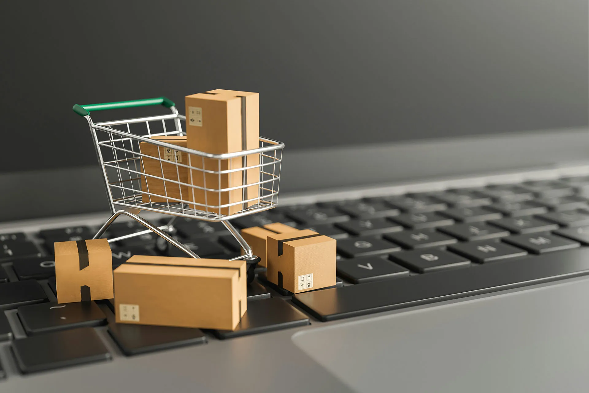  Mini shopping cart filled with cardboard packages on a laptop keyboard, representing online shopping and e-commerce delivery.