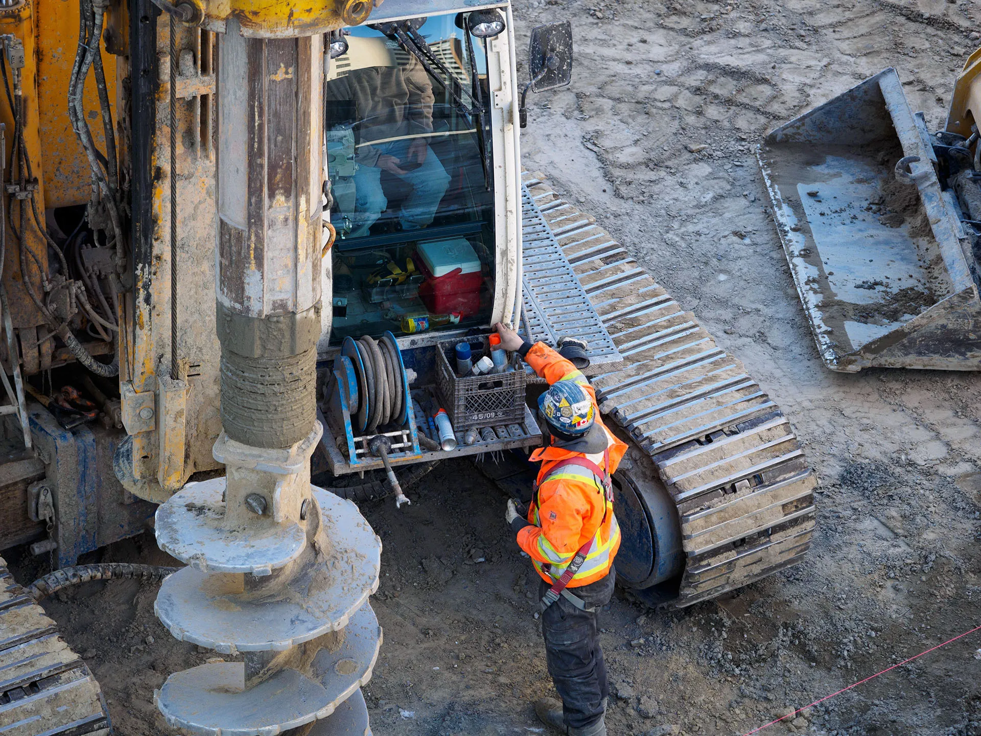  Construction worker cleaning heavy drilling equipment with a pressure washer at an active job site.