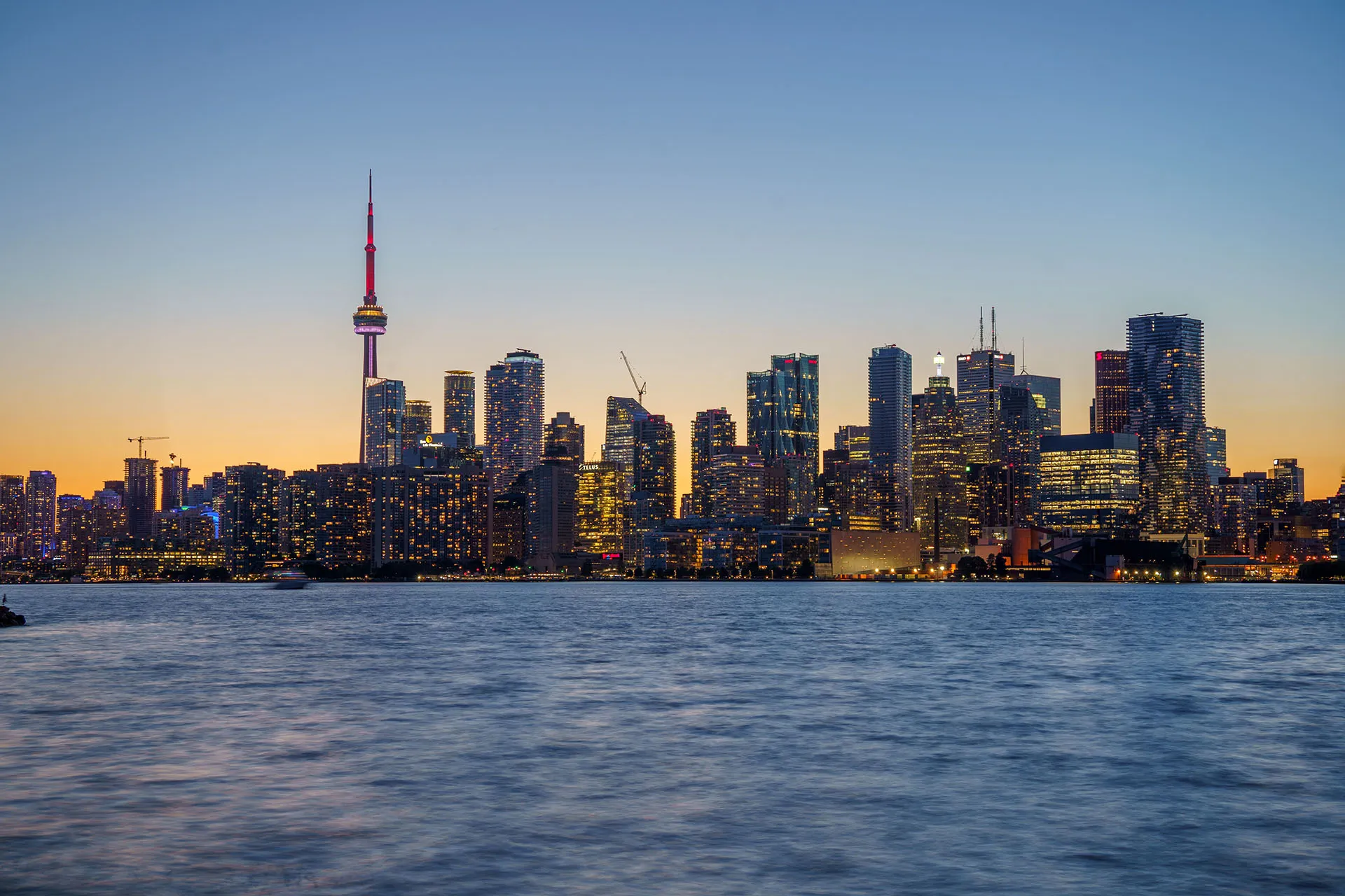  An elevated view of the Toronto financial district skyline at dusk, highlighting illuminated office skyscrapers and the CN Tower over blue water.