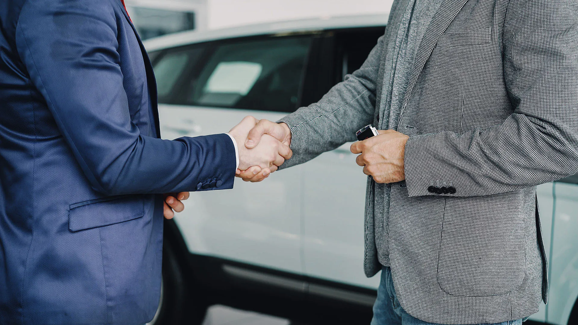  Two business professionals shaking hands in a dealership or vehicle handover setting.