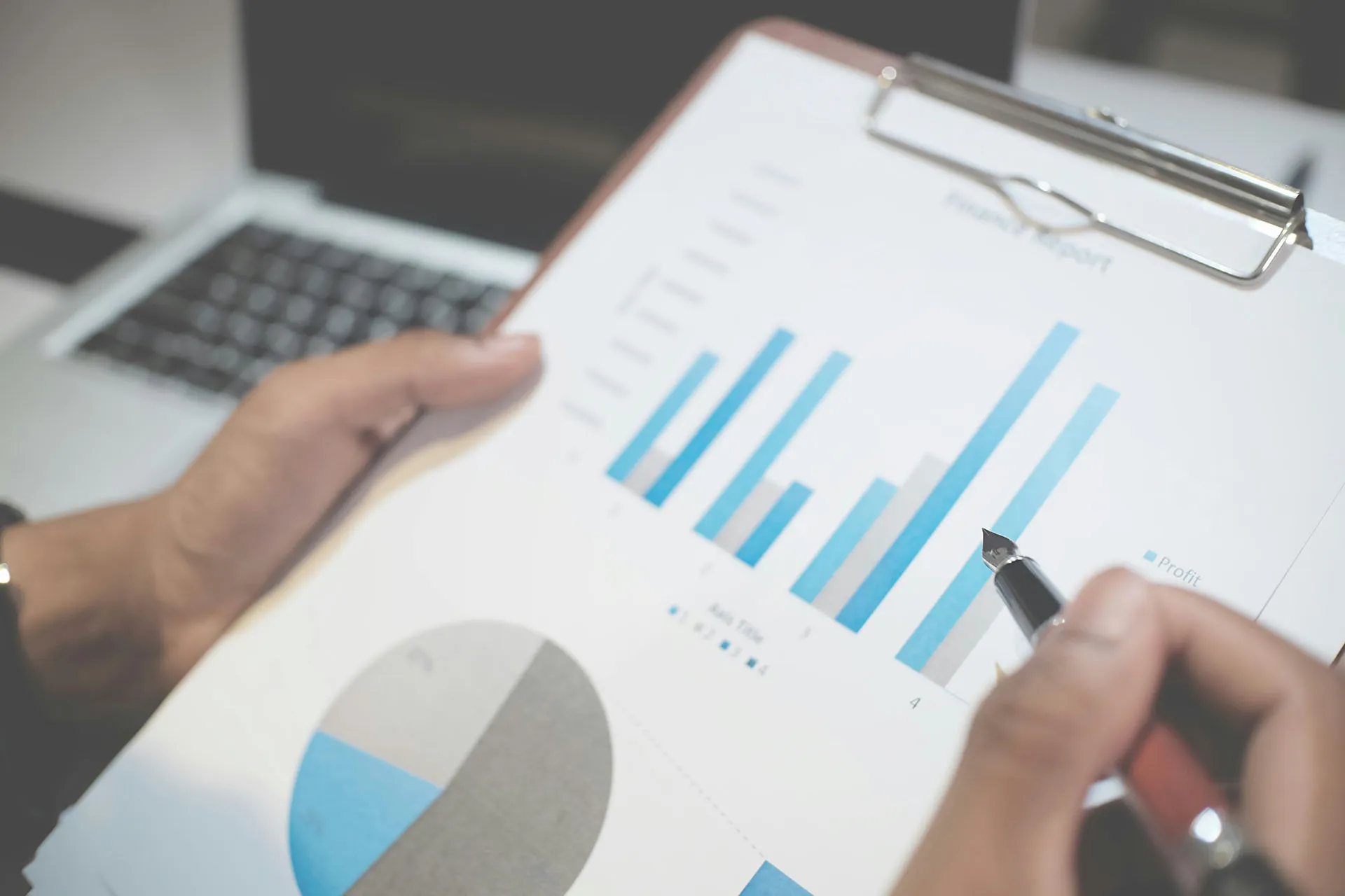  A close-up shot of an analyst using a fountain pen to point at blue bar charts and a pie graph on a clipboard financial report.