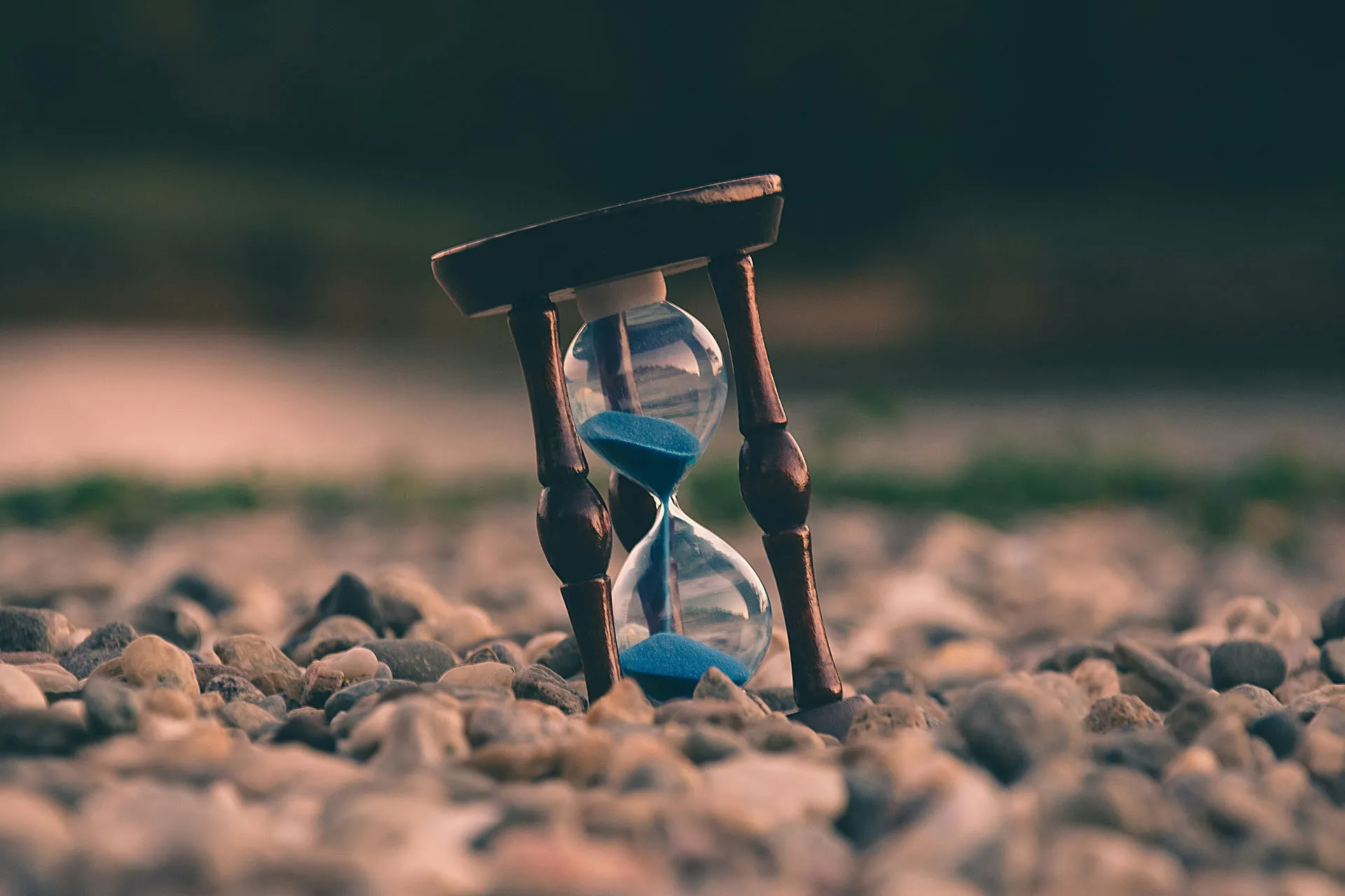 Hourglass with blue sand resting on small rocks, representing time passing, deadlines, or patience.