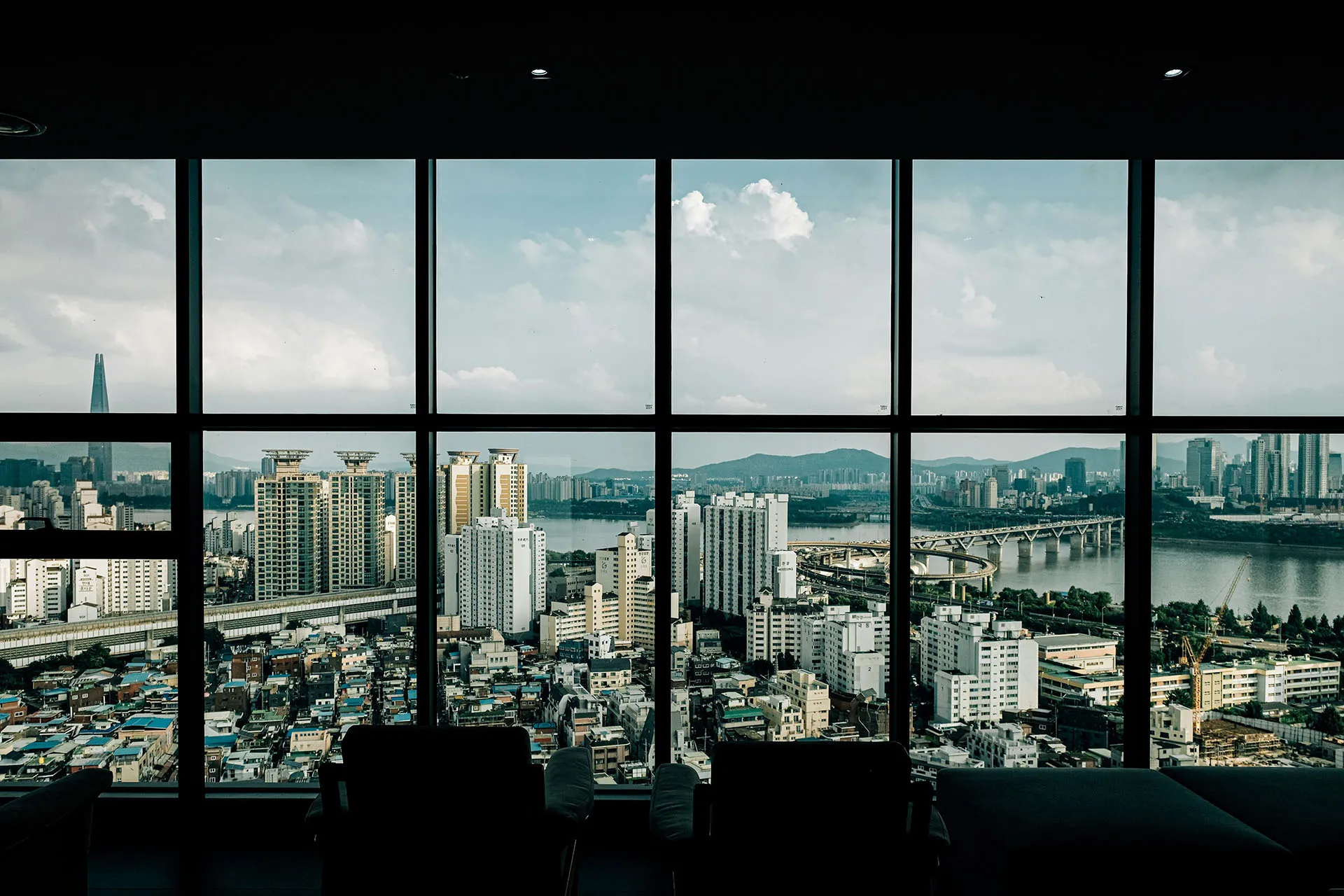  A wide-angle view of a sprawling city skyline and river seen through a large modern office window with silhouetted chairs in the foreground.