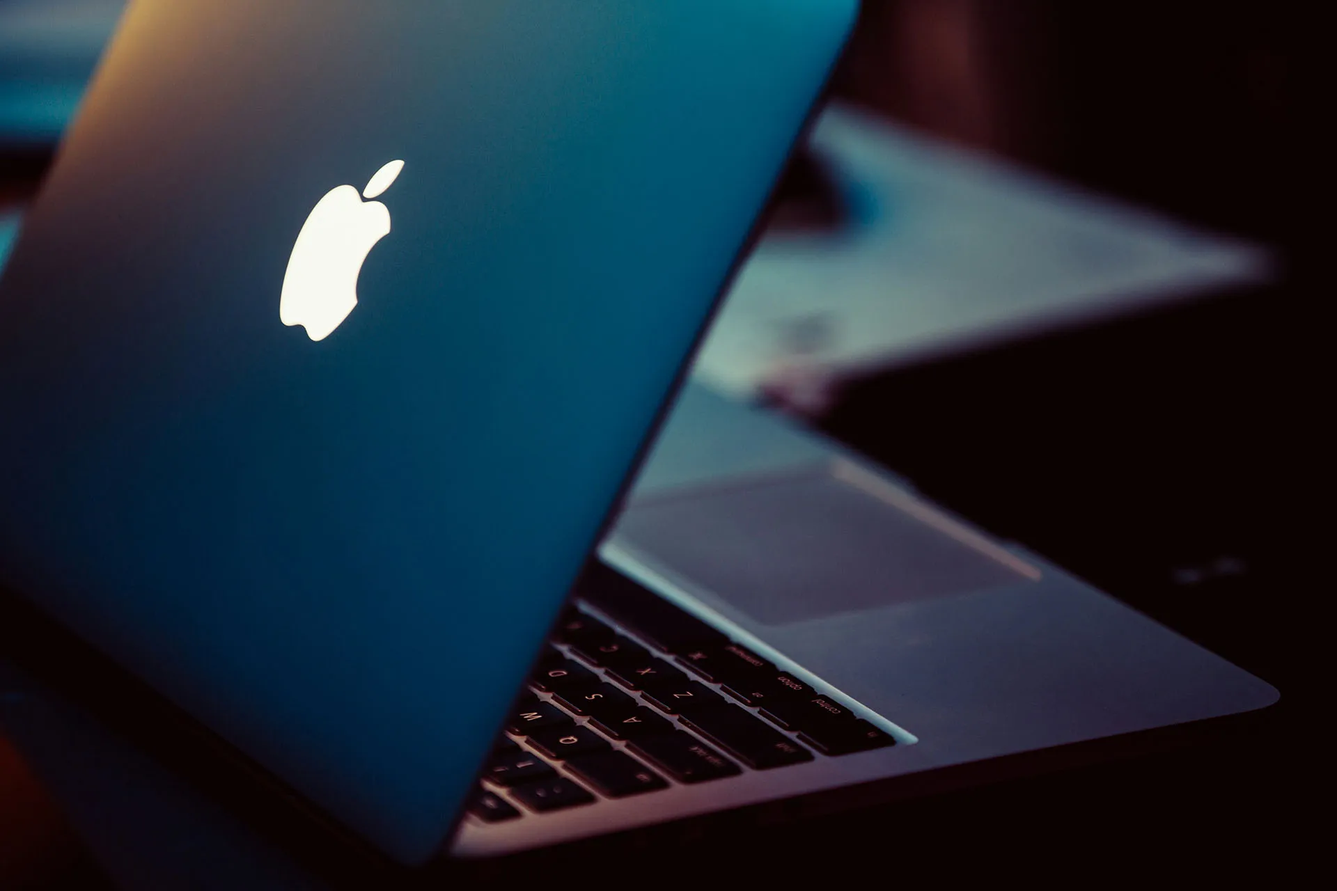 Close-up of an open Apple MacBook with the illuminated Apple logo in a dark, moody setting.