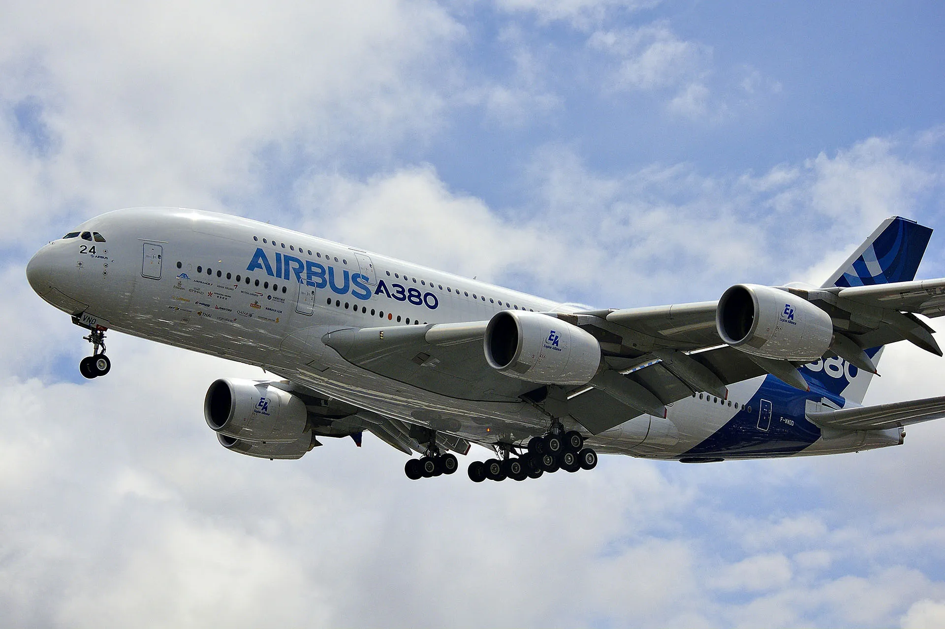  Airbus A380 aircraft flying through a cloudy blue sky with landing gear extended.