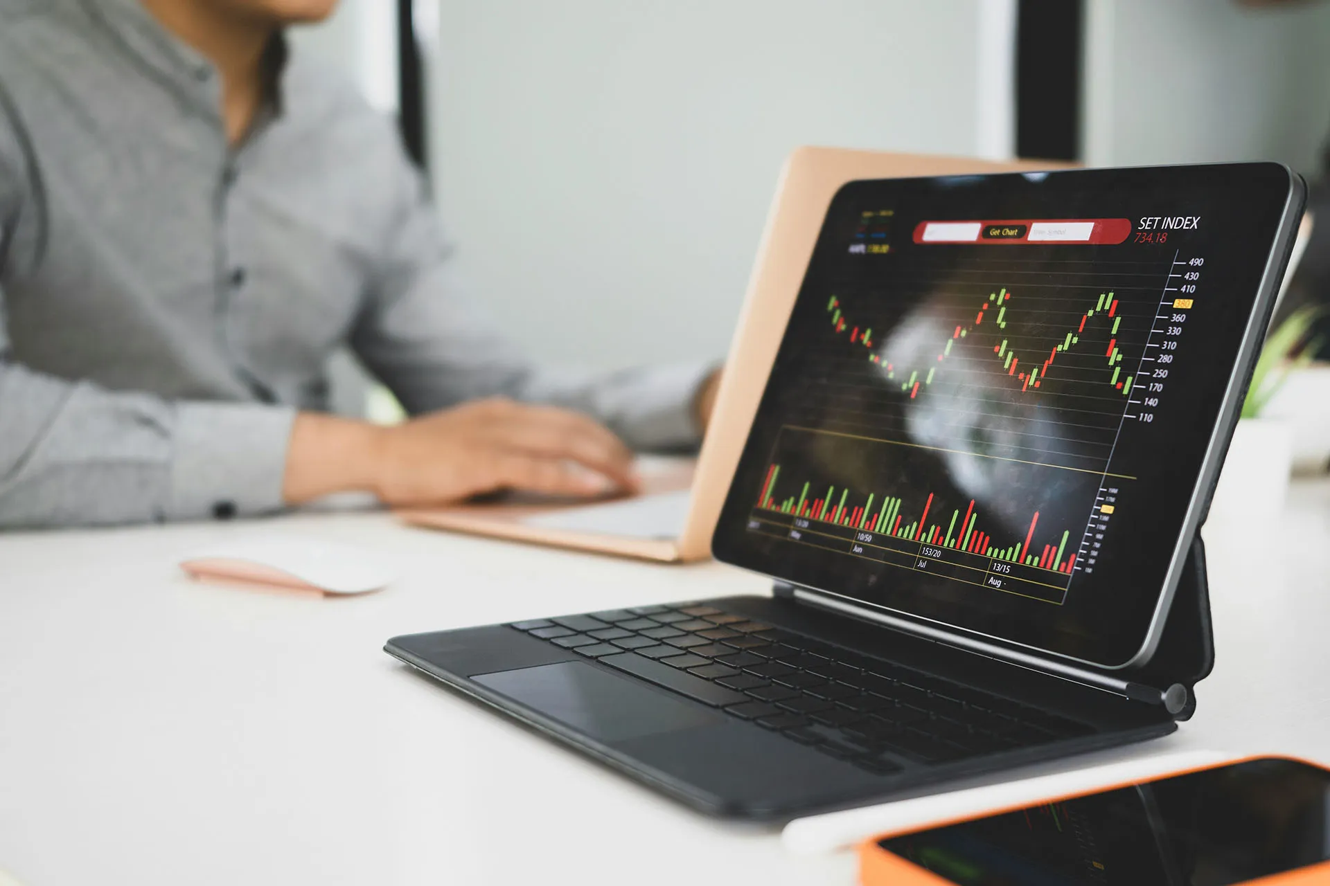  A computer tablet and desktop screen displaying financial statistics, graphs, and data charts