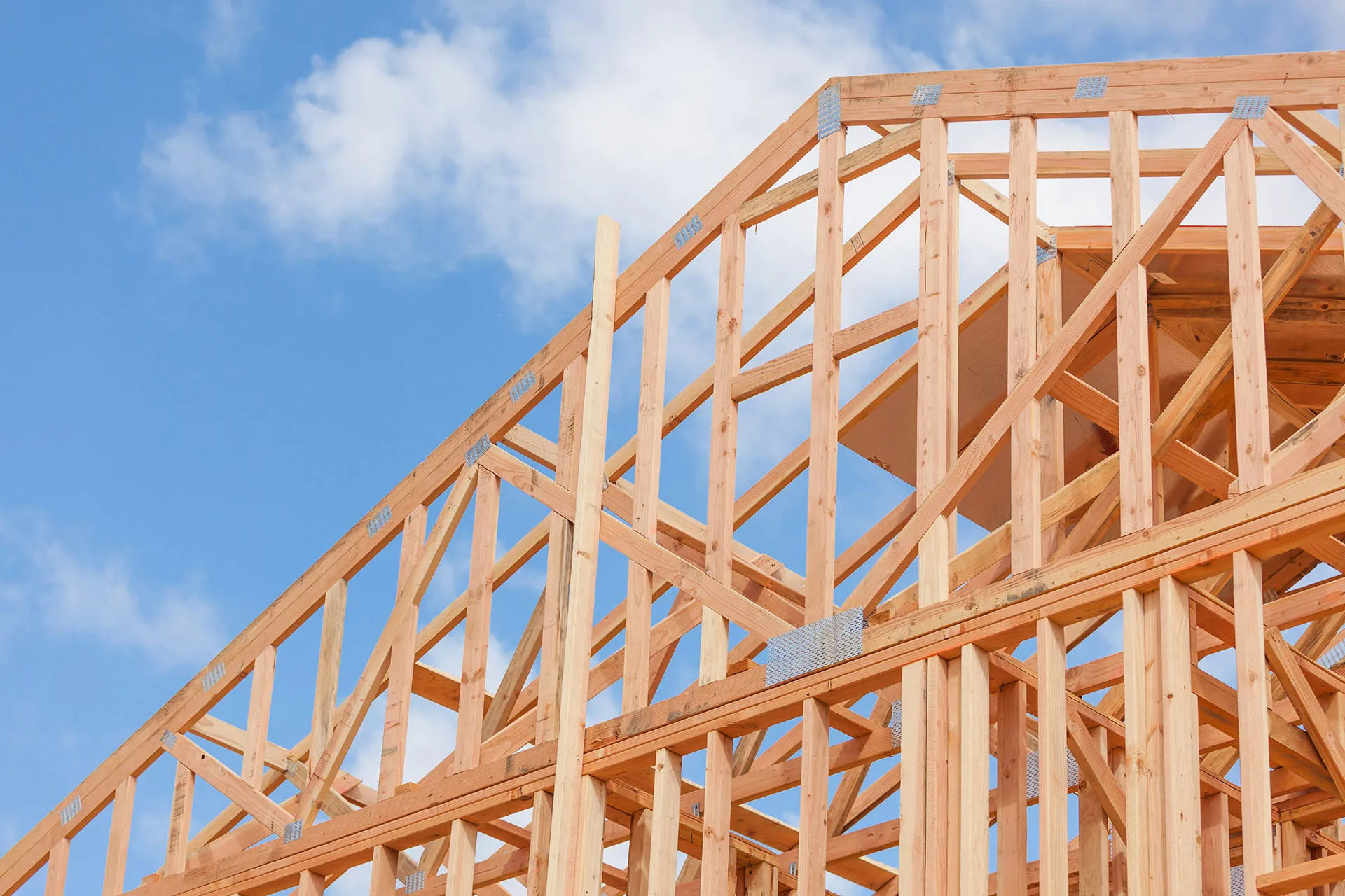  Wooden framing of a new building under construction against a blue sky with clouds.