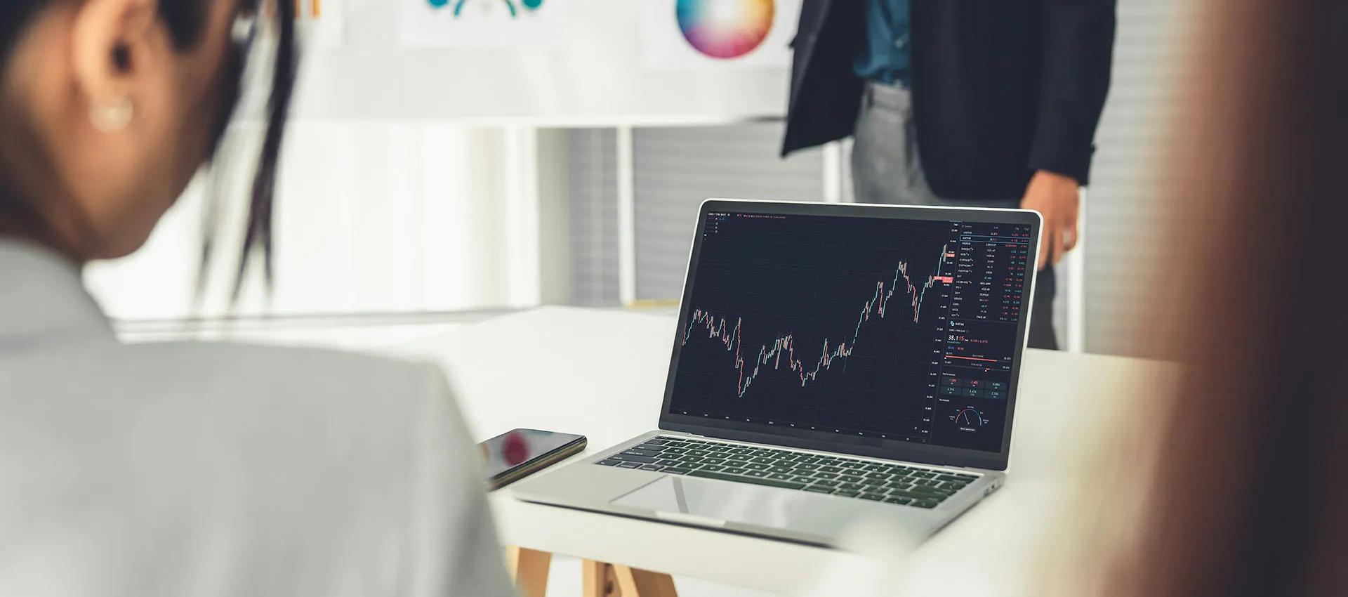  Business professional analyzing stock market data on a laptop during a team meeting in a modern office.