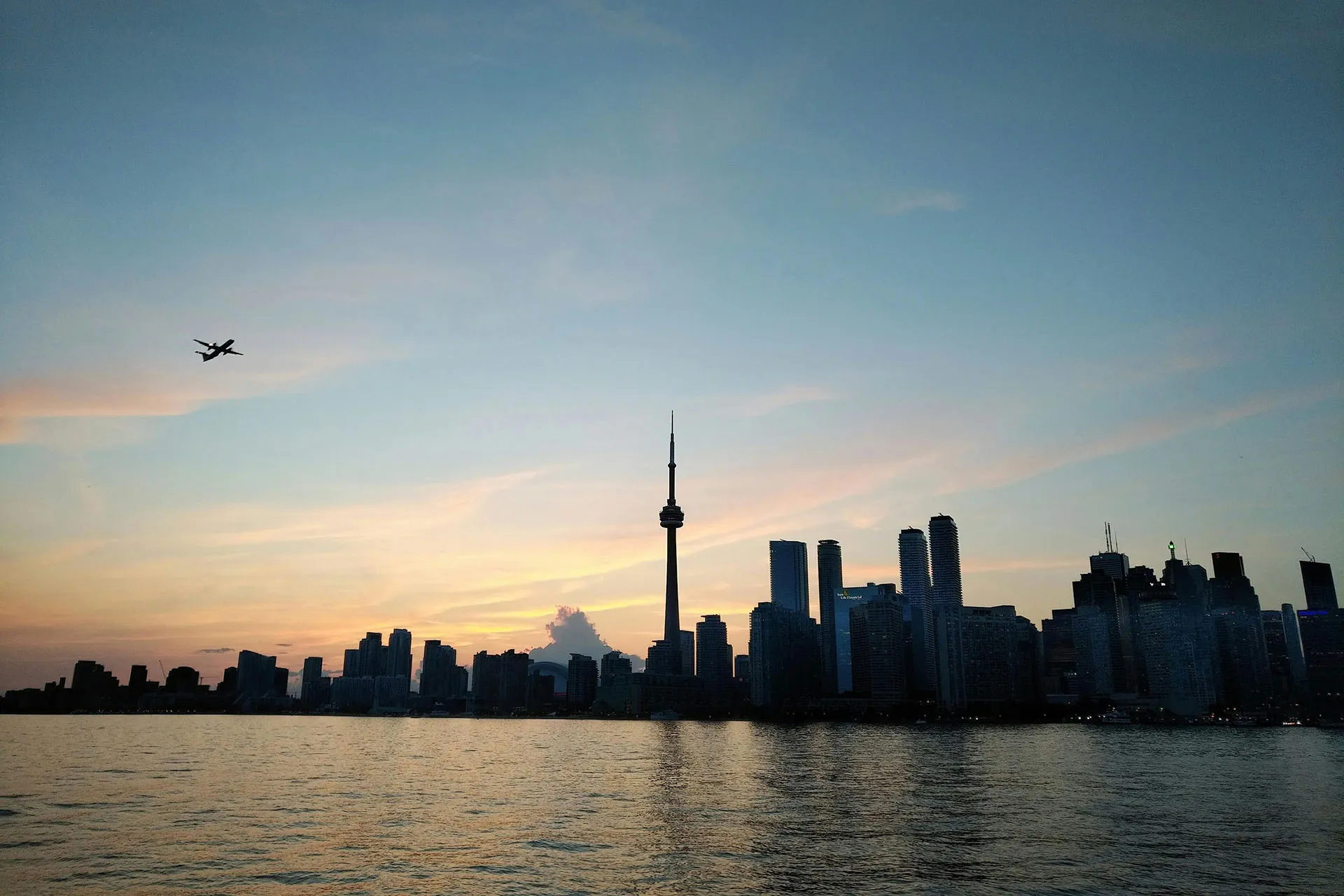  Toronto skyline at sunset with the CN Tower overlooking the waterfront and a plane flying overhead.
