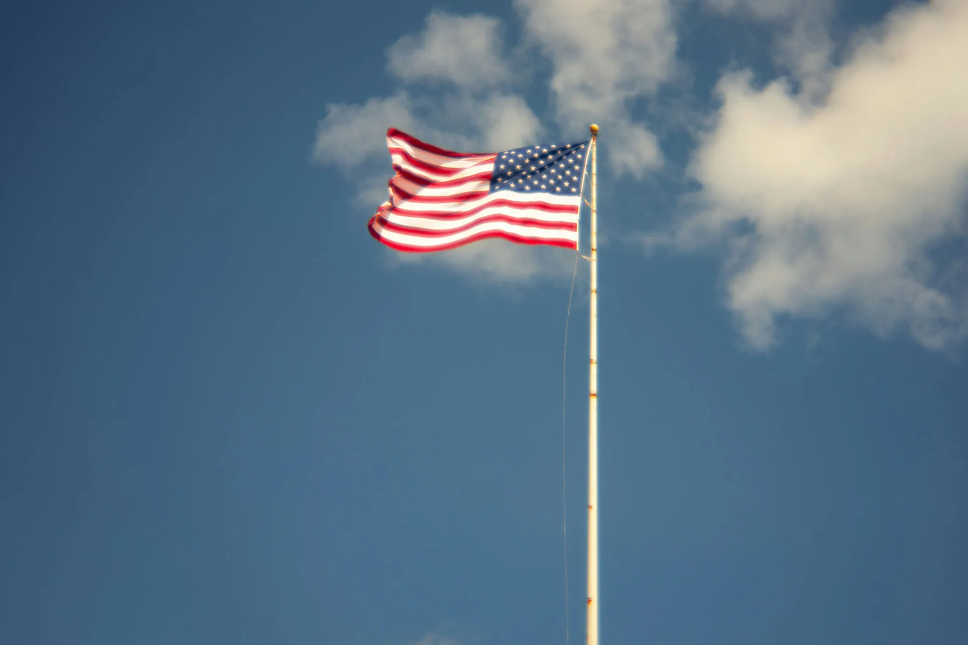  An American flag blowing against a blue sky with clouds