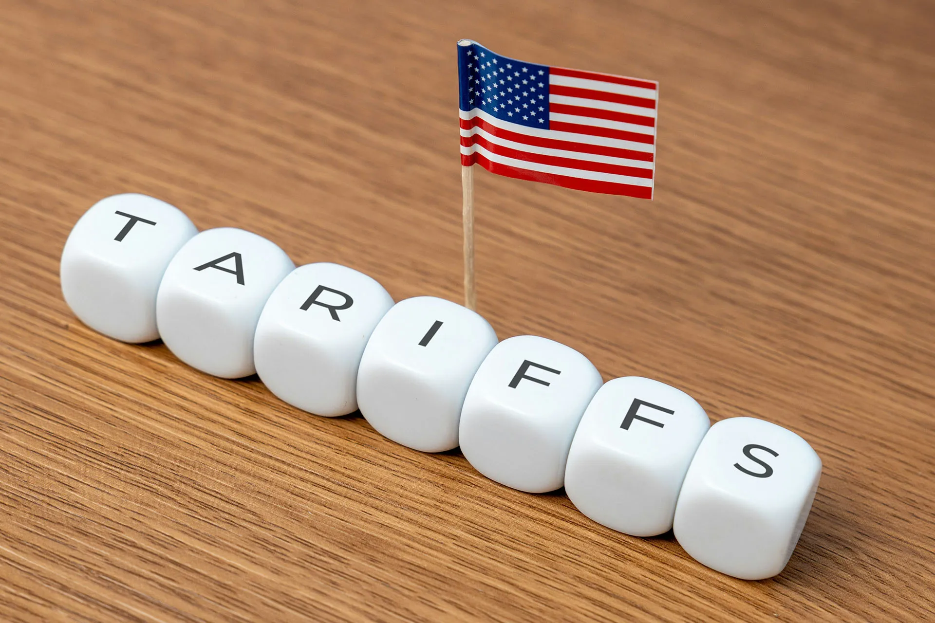  White letter blocks spelling “TARIFFS” on a wooden table with a small American flag.