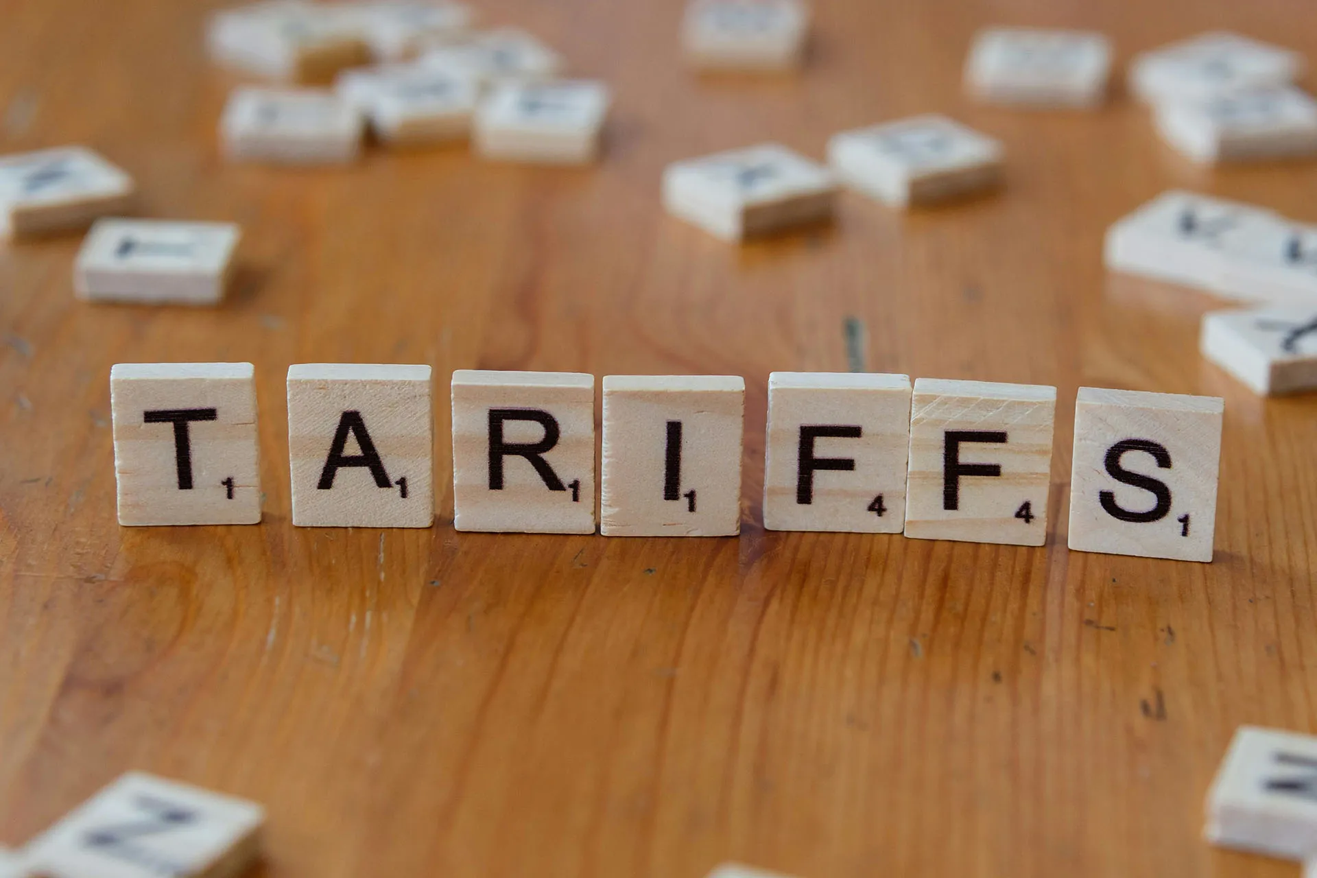 Scrabble pieces standing on a table spelling out the word "Tariffs"