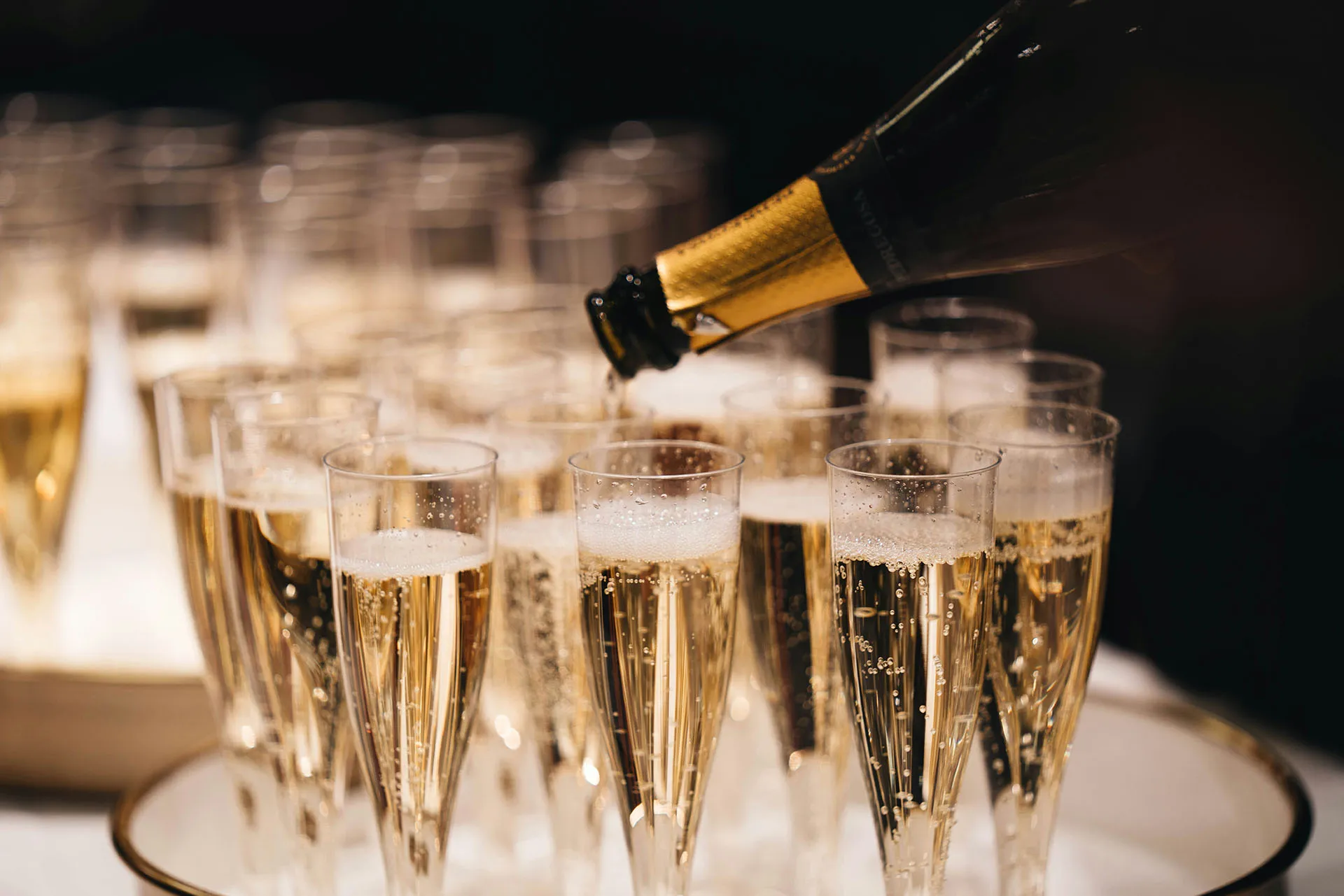 Champagne being poured into a row of flute glasses for a celebration or formal event.