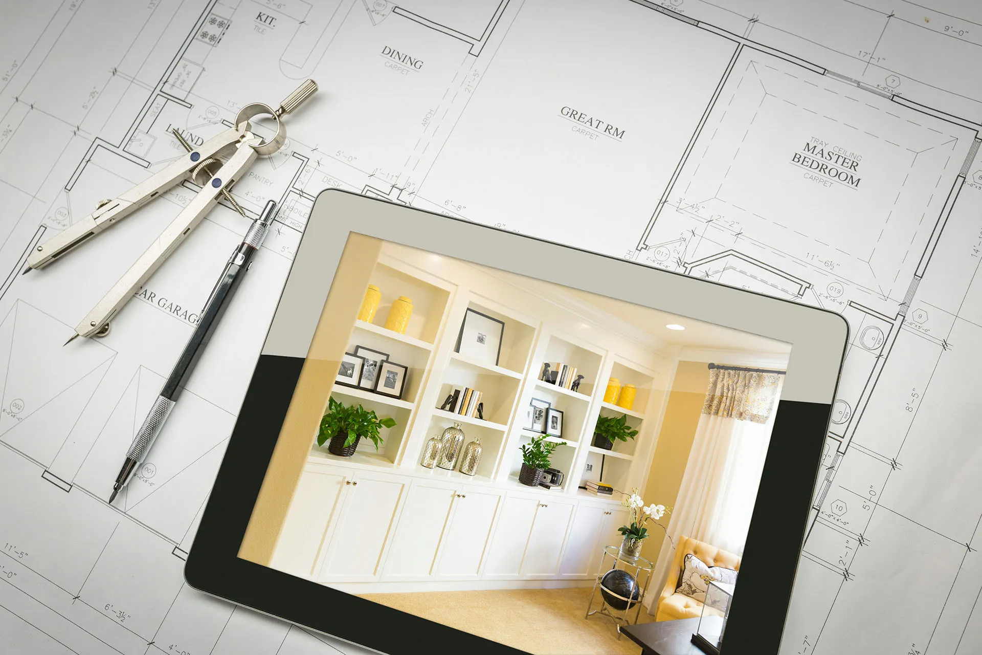 A digital tablet displaying a living room, sitting on top of white blueprints for a house beside measuring tools and a pencil