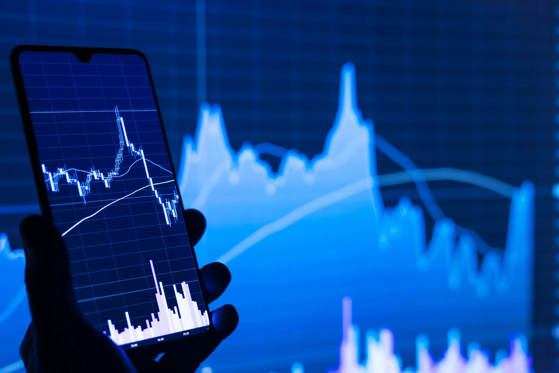 Smartphone with a financial trend graph in front of large blue screen out of focus showing the same