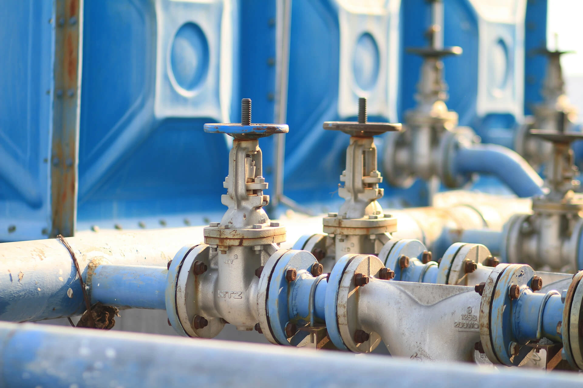 A network of metal pipes with blue screw knobs in front of large blue plastic containers