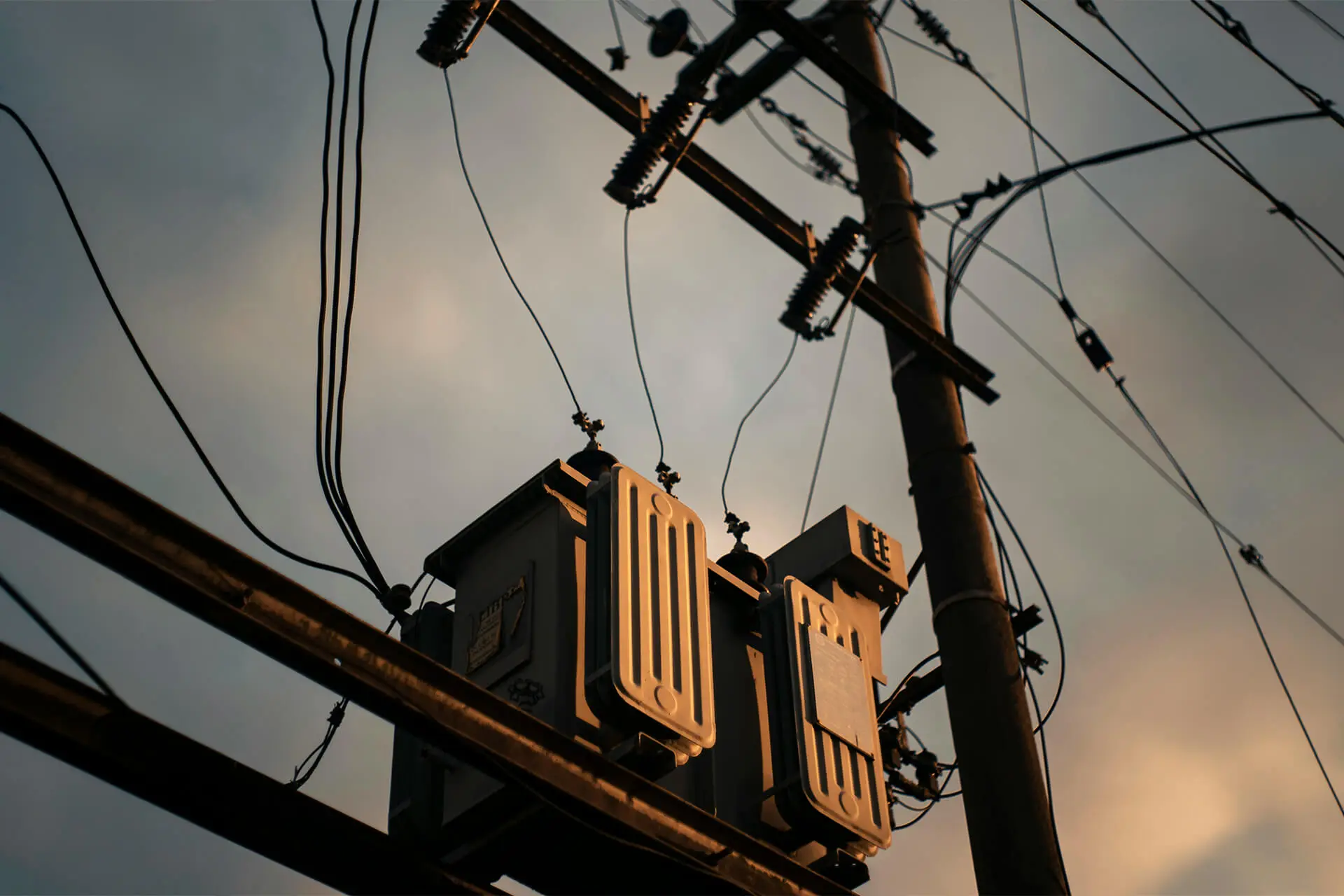 Electrical transformer attached to an electrical pole and powerline at sunset with pale clouds in the background