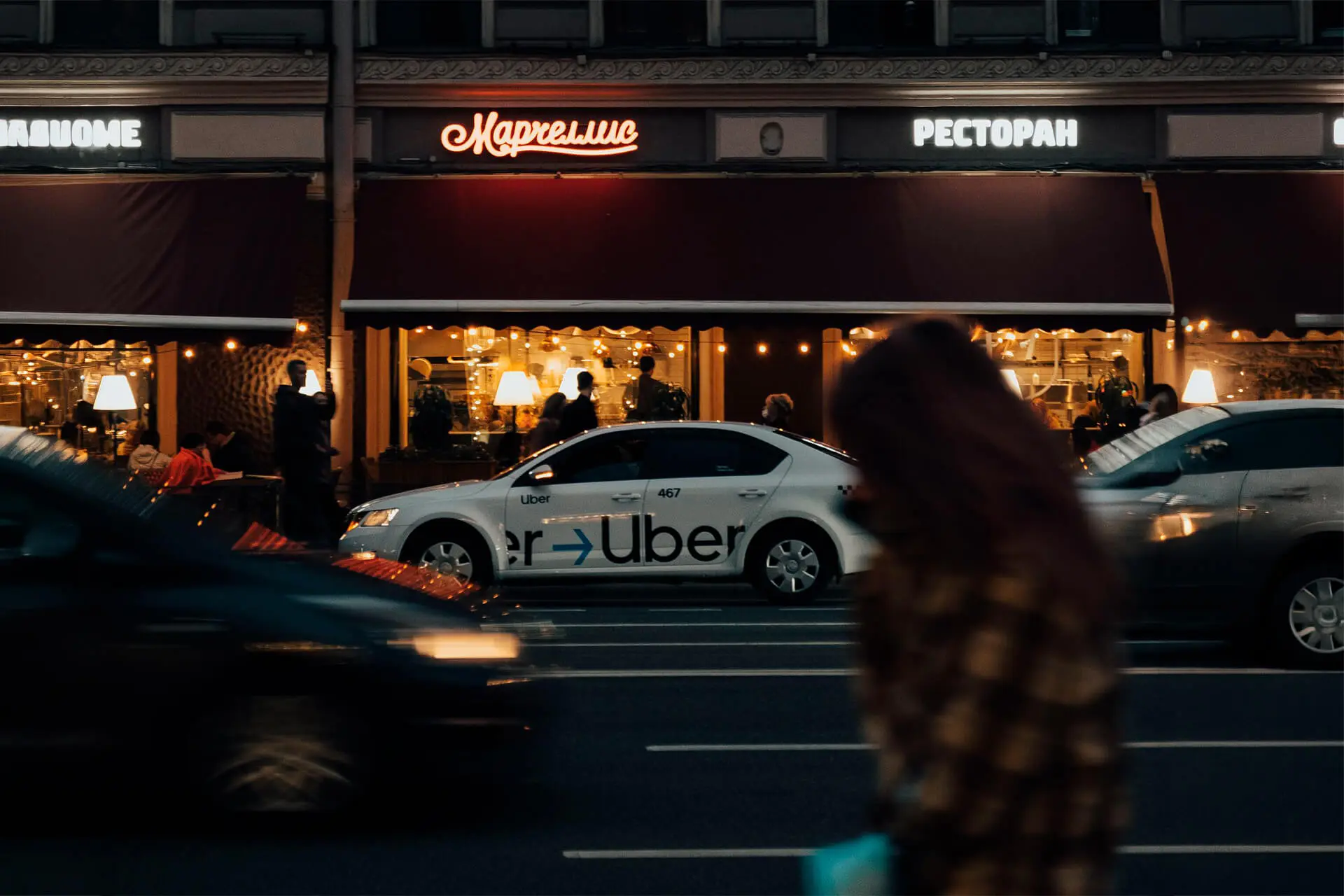 Uber car parked on a busy city street outside a lit restaurant at night.