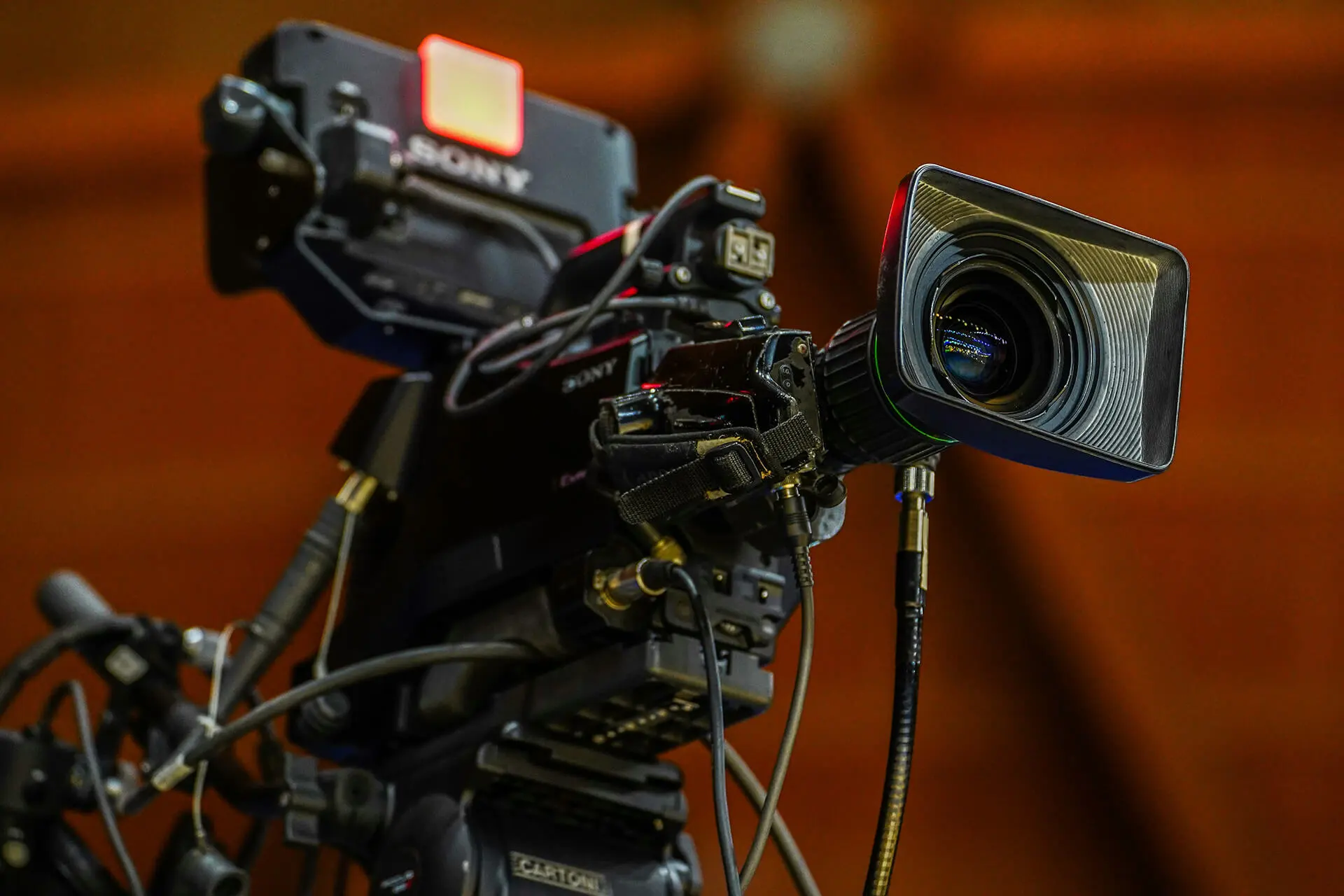 Professional video camera on a tripod with a large lens, set up for filming in an indoor studio or event space.